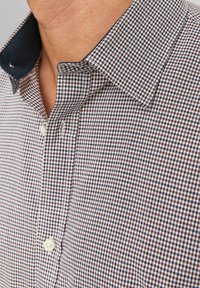 Rutigt skjorta i vitt, brunt och marinblått, med en knapp-ned krage och ett texturerat tyg med ett subtilt mönster.