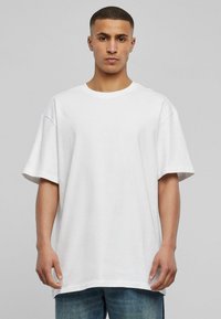 Biely oversized tričko z bavlny, s okrúhlym výstrihom, krátkymi rukávmi a voľným strihom, v kombinácii s modrými džínsami.