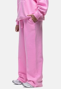 Roze, oversized sweatshirt en broek van zacht materiaal. Heeft een voorvak en contraststiksel. Gemaakt met grijze sportschoenen.