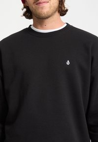 Sort crewneck sweatshirt lavet af bl�ødt stof, med et lille hvidt logo på venstre bryst, afslappet pasform og ribbet krave.