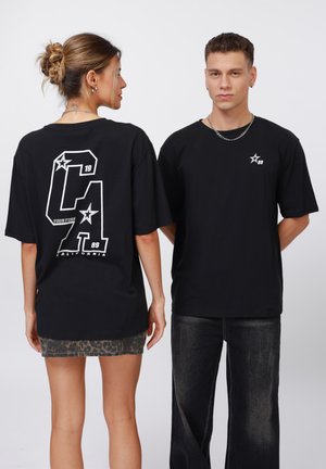 Sorte bomulds T-shirts med hvide grafiske designs; en har et stort "CA" på ryggen og et lille logo på fronten. Standard pasform.