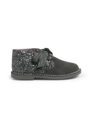 Bota de ante negra con un panel de lentejuelas negras brillantes en el tobillo, con suela plana y un lazo de cinta de tela en la parte delantera.