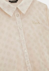 Blusa rosa pallido con colletto, caratterizzata da un motivo sottile e chiusura a bottoni. Logo dorato "Guess" ricamato sul lato sinistro.