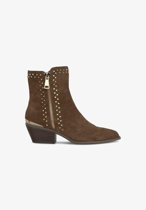 Botte de cheville en daim marron avec un bout pointu, une fermeture éclair dorée et des accents cloutés sur le côté. Présente un talon en bois empilé bas.