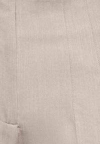 Tissu beige avec des coutures visibles verticales et horizontales et une surface légèrement texturée.