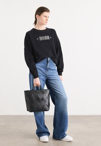 Felpa nera con grafica "BOSS", jeans blu a vita alta e una borsa nera intrecciata. Sneakers bianche completano l'outfit.