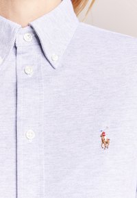 Light blue button-up shirt made of textured fabric, featuring a small embroidered horse logo on the left chest area.