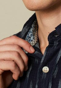Marineblauw shirt met een patroon op de kraag; voorzien van een knoopsluiting en een textuurstof met subtiele strepen en contrasterende details op de binnenkraag.