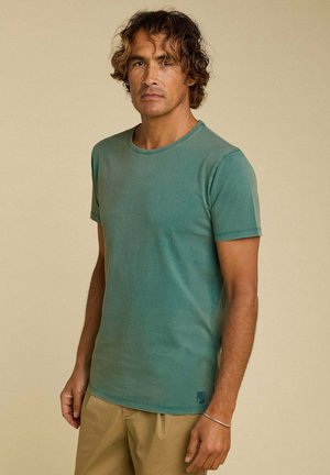 T-shirt teal à manches courtes en coton doux, décolleté rond, design légèrement ajusté, avec un petit logo imprimé près de l'ourlet.