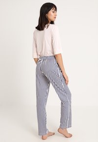  Lichtroze top met driekwartmouwen en loszittende broeken met blauwe strepen. De stof lijkt glad met een elastische tailleband.