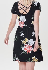 Robe trapèze florale en tissu noir. Manches courtes, bretelles croisées dans le dos, fleurs vibrantes jaunes, rouges et blanches ; texture lisse.