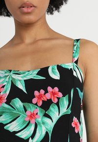 Haut floral avec un fond noir, présentant des fleurs roses et des feuilles vertes. Encolure carrée, bretelles fines et tissu respirant.