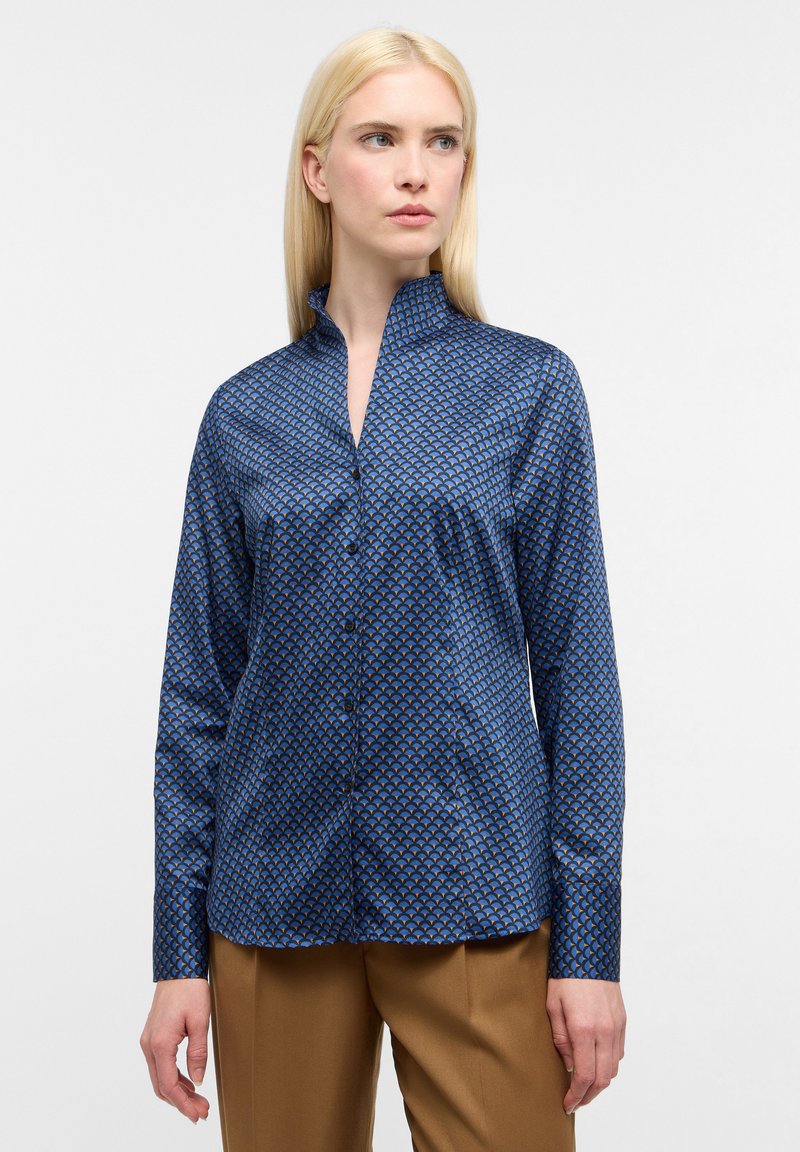 Camicia blu a fantasia con colletto alla coreana, maniche lunghe e chiusura a bottoni. Presenta un design geometrico in diverse tonalità di blu e beige.