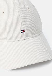 White corduroy cap featuring a stitched logo in red, white, and navy. The design includes ventilation holes and a curved brim.