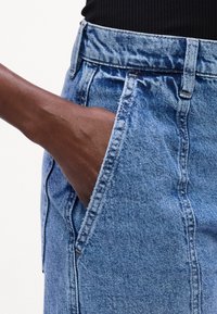Jeans de mezclilla azul claro con cintura alta, que cuentan con bolsillos laterales y un ajuste ligeramente holgado. Textura suave, diseño clásico de cinco bolsillos.