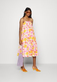 Vestido de verão floral em rosa e amarelo, feito de tecido leve, com um formato fluido e alças finas. Combinado com óculos de sol laranja e uma mala lavanda.