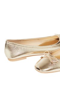 Ballerine metalliche oro con punta arrotondata, suola piatta e dettaglio a fiocco davanti. Texture liscia con una finitura lucida.