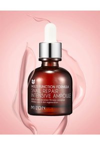 Botella cuentagotas de vidrio marrón con tapa plateada. La etiqueta dice "Fórmula Multifuncional Ampoule Intensiva de Reparación de Caracol". Fondo de líquido rosa.