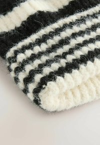 Wollen gebreide deken met een gestreept patroon in zwart en roomkleur, voorzien van een zachte, textuurrijke afwerking en zichtbare fuzzy vezels langs de randen.