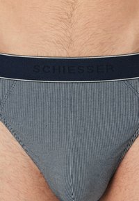 Mutande a fascia in tessuto a righe blu navy e bianche con una fascia elastica a contrasto con la scritta "Schiesser" in rilievo, che mostra una texture liscia e un design aderente.