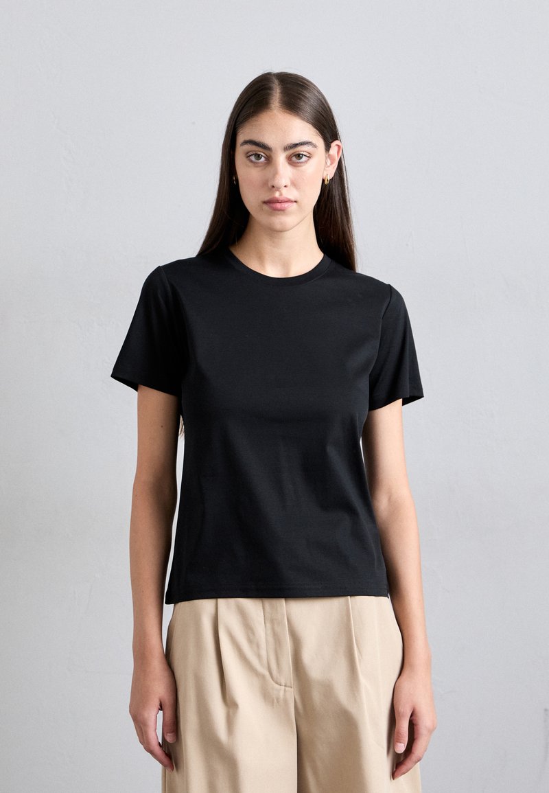 Black cotton t-shirt with a round neckline and short sleeves, featuring a slim fit and smooth texture. Paired with light beige pants.