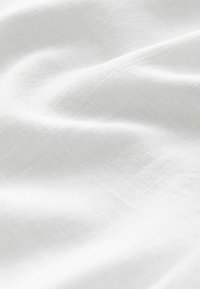Bílá látka s hladkým, mírně texturovaným povrchem. Měkký splývavý efekt a jemná průsvitnost jsou patrné v záhybech a vráskách.