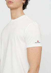 T-shirt bianco in cotone con collo a giro e maniche corte. Presenta un logo Peuterey nero e rosso sulla manica sinistra. Tessuto liscio.