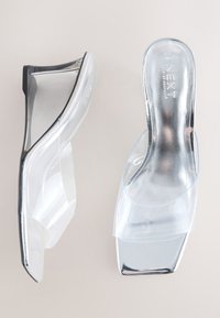 Sandale s prozirnom potpeticom s transparentnim remenom, sjajnim srebrnim detaljima, otvorenim prstima i elegantnom potpeticom u obliku kile.