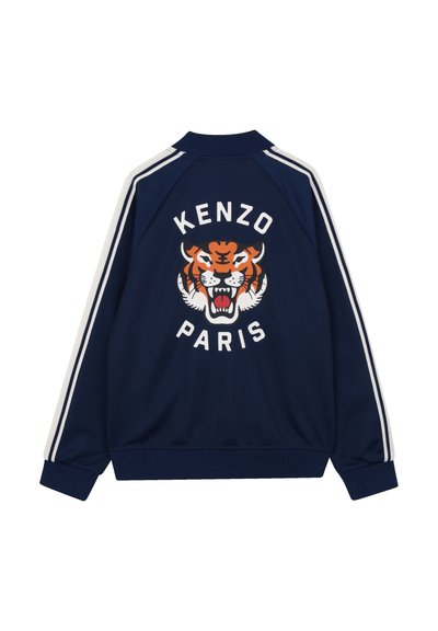 Marineblauw trainingsjack met witte strepen, met een oranje en zwarte tijgerafbeelding en de tekst "KENZO PARIS" op de achterkant. Gladde stof.