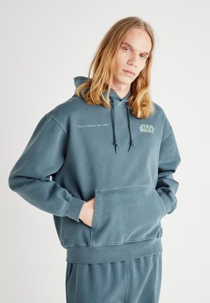 Felpa con cappuccio di colore blu teal, realizzata in tessuto morbido. Presenta una tasca frontale, la scritta "Non dirmi mai le probabilità" e il logo "STAR WARS" sul petto.