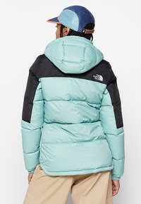 Padded jakna u mint zelenoj i crnoj boji, s kapuljačom, kviltanom teksturom i logotipom na gornjem lijevom dijelu leđa. Glatka tkanina.