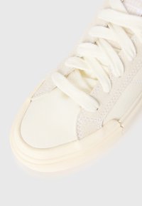 Off-white lerret sneakers med tykke snører, gummitåhette, og synlige sømmer på en enkel hvit bakgrunn.