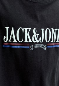 Μαύρο ύφασμα με λευκό κείμενο "JACK & JONES" πάνω από κόκκινες και μπλε οριζόντιες ρίγες και μια μικρή σημαία "19 ORIGINALS 90".