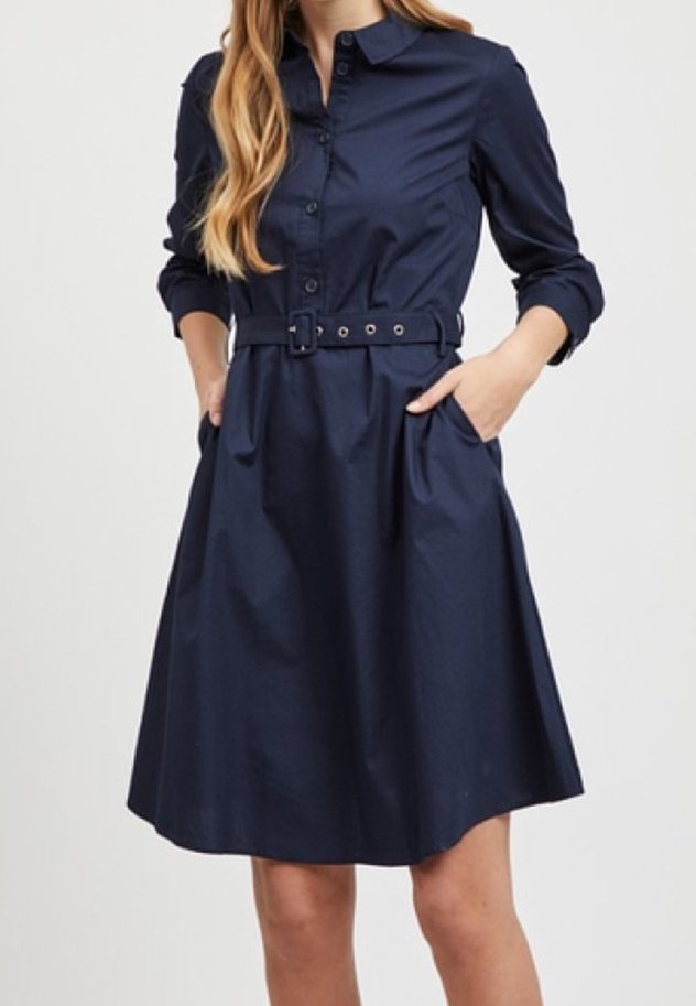 Marinblå skjortklänning med krage, framknäppning, långa ärmar och bälte i midjan. Utsvängd kjol med sidofickor. Blandning av bomull.