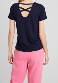 Camiseta de manga corta azul marino con escote redondeado en la parte posterior y detalle de tiras entrelazadas. Combinada con pantalones de pierna ancha rosa de cintura alta.