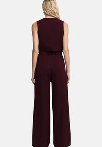 Tuta bordeaux senza maniche, con pantaloni a gamba larga e cintura in vita, realizzata in un tessuto liscio e strutturato.