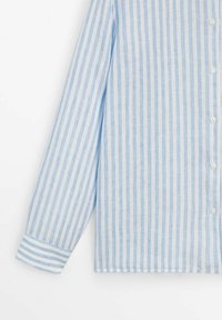 Chemise à manches longues boutonnée avec des rayures verticales bleu clair et blanc et des poignets assortis rayés sur un fond blanc uni.