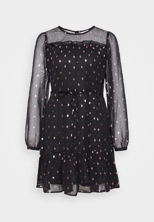 Robe noire avec des manches longues transparentes, un col froncé et une jupe à volants. Présente un motif à pois métalliques et un lien à la taille.
