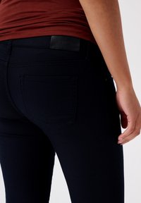 Mörkblå denimjeans med en slät textur, med en bakficka och en märkeslogotyp i svart läder vid midjan.