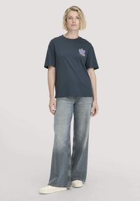 Navy katoenen t-shirt met een ronde hals, korte mouwen en een paarse bloemenprint op de linkerborst, gecombineerd met wijde, vervaagde spijkerbroeken.