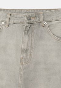 Jean en denim gris clair en gros plan montrant la ceinture, le bouton métallique, les passants de ceinture et les poches avant avec des coutures en contraste.