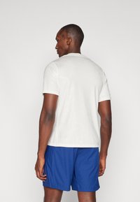 Hvid kortærmet skjorte med diskret "Air Jordan" mønster, parret med blå strukturerede shorts. Pasformen er afslappet og behagelig.