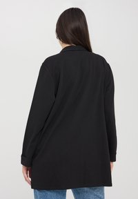 Blazer nero a maniche lunghe con collo, vestibilità morbida e polsini con bottone. Tessuto liscio con orlo dritto.