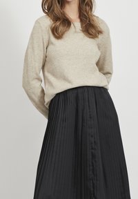 Beige gebreide trui met lange mouwen, gecombineerd met een zwarte geplooide rok met een gladde textuur en verticale plooien.