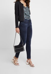 Černá krátká bunda, tyrkysový top s leopardím potiskem, tmavě modré úzké džíny, bílé sandály na ramínka a černá kabelka s korálky.