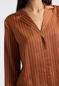 Brąsowa koszula z długim rękawem w różowe pionowe paski, z kołnierzem z wycięciem i zapięciem na guziki. Gładka tekstura i dopasowany krój.