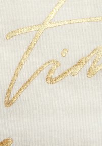 White fabric with a ribbed texture featuring decorative golden cursive lettering. The design includes smooth and shiny accents on a neutral background.