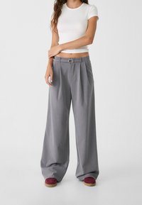 Pantalons gris taille haute à jambe large avec des plis, comportant une passante de ceinture et une petite boucle, fabriqués en tissu lisse et léger.