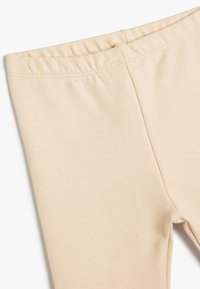Leggings beige con una cintura elástica, que presentan una textura suave y un diseño ajustado, fabricados con tejido elástico para mayor comodidad.