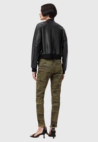 Zwarte leren bomberjack met geribbelde manchetten, gecombineerd met camo cargo-broek met zakken en ritsen aan de onderkant, en zwarte hakken.